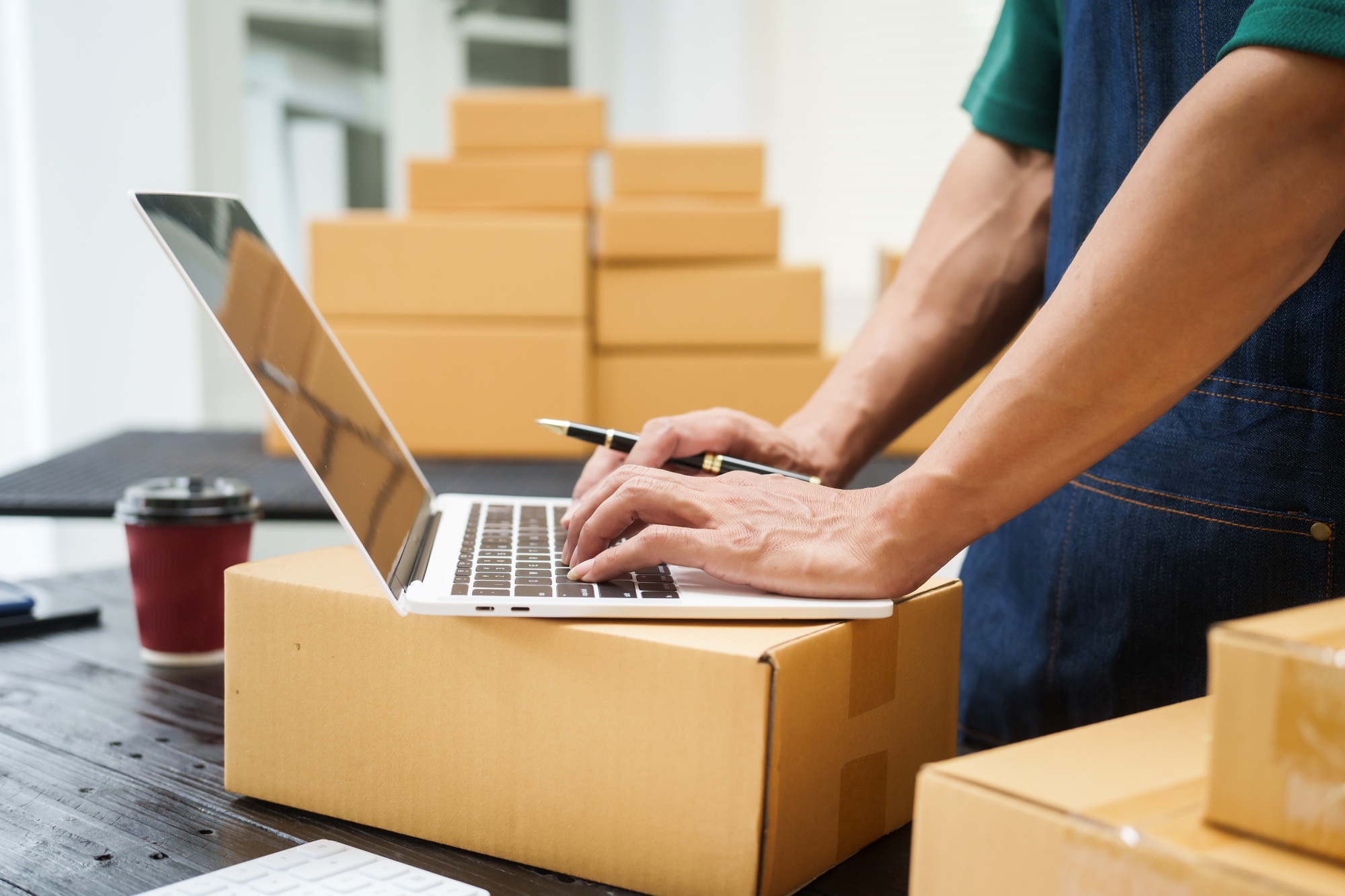A man is working at his desk, preparing parcel boxes for shipment. He checks packs items carefully