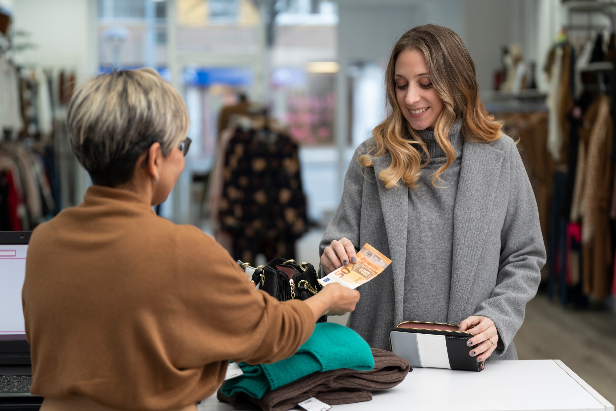 Young blonde woman paying in cash at the clothing store with a fifty euro bill